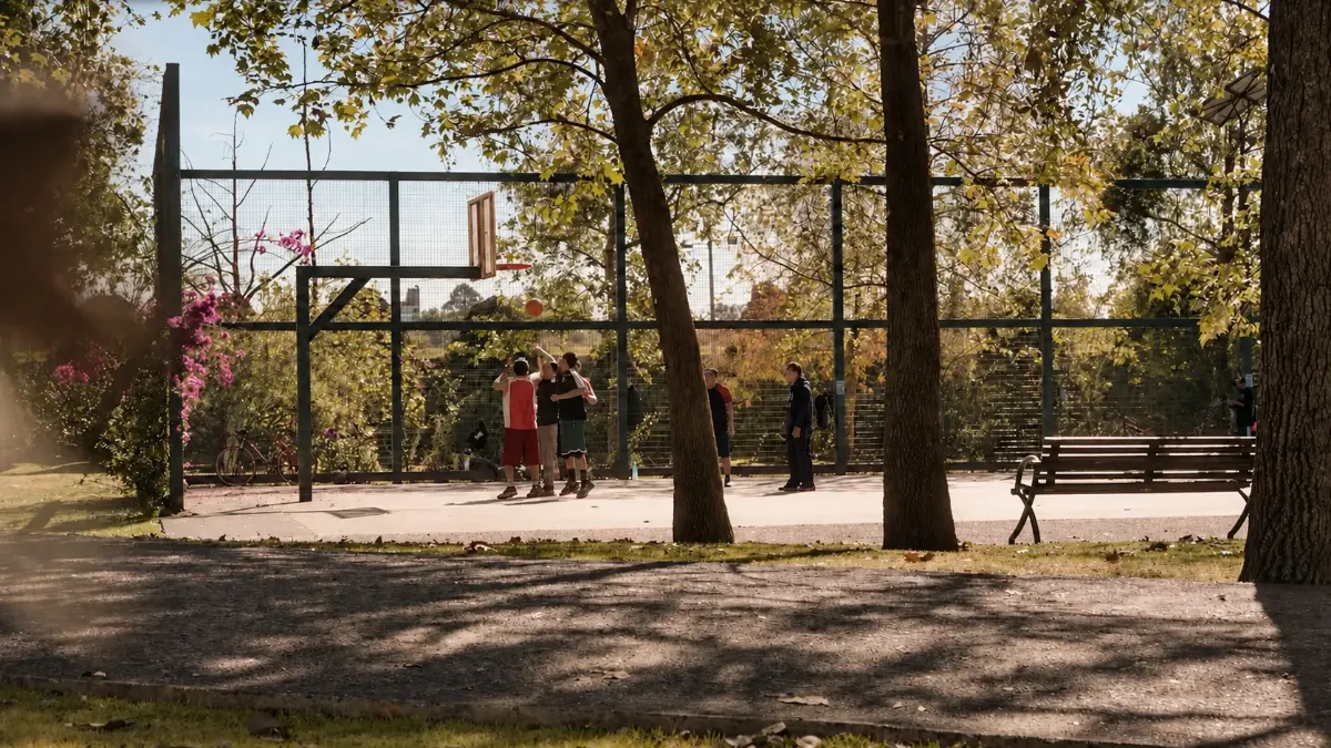 Una house juega basquetbol en una cancha rodeada de árboles en un parque