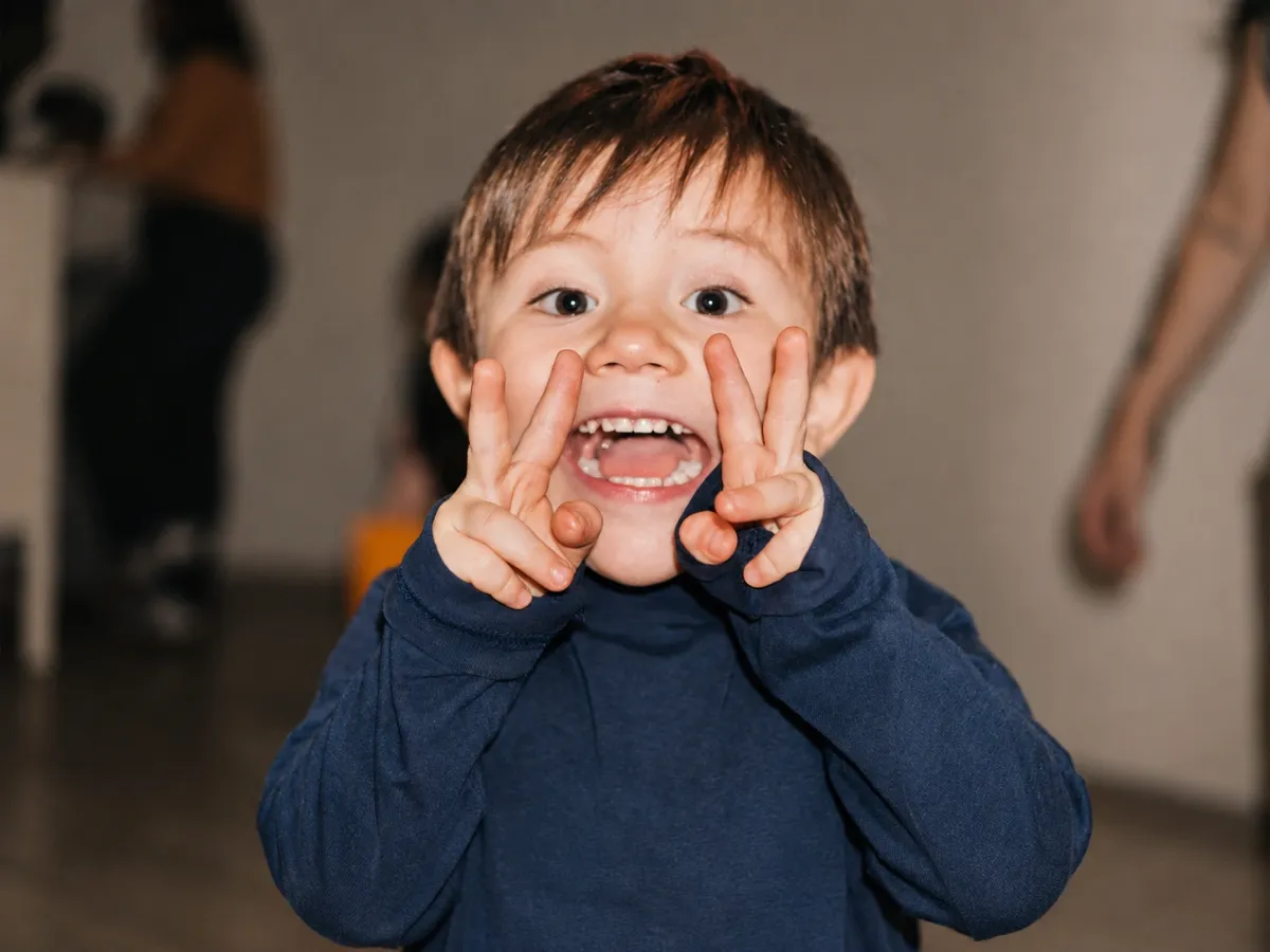 Niño sonriente hace caras divertidas con las manos durante Mosaic Kids